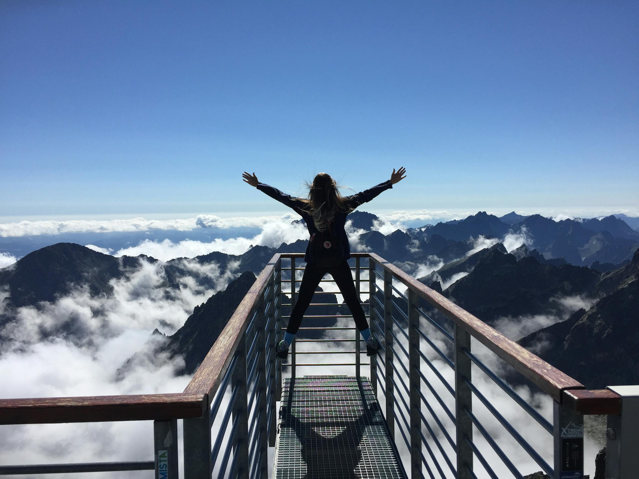 A woman on a lookout bridge looking at mountains and blue sky.